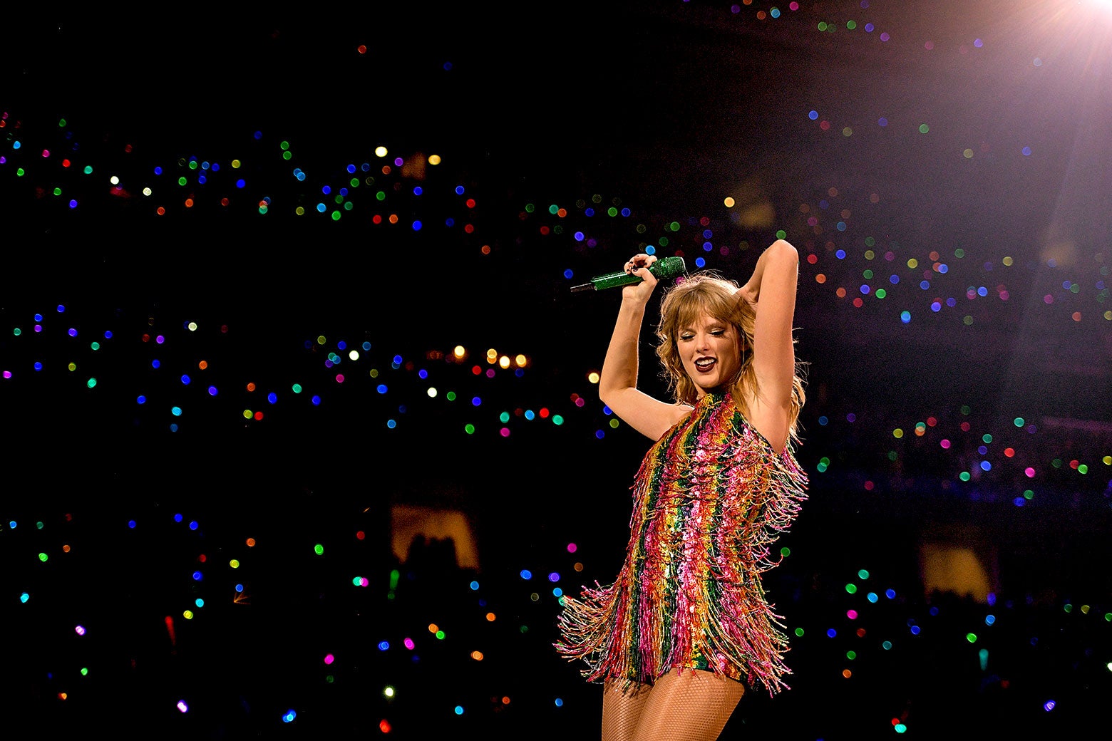 Taylor Swift in a striped dress dances in a stadium.