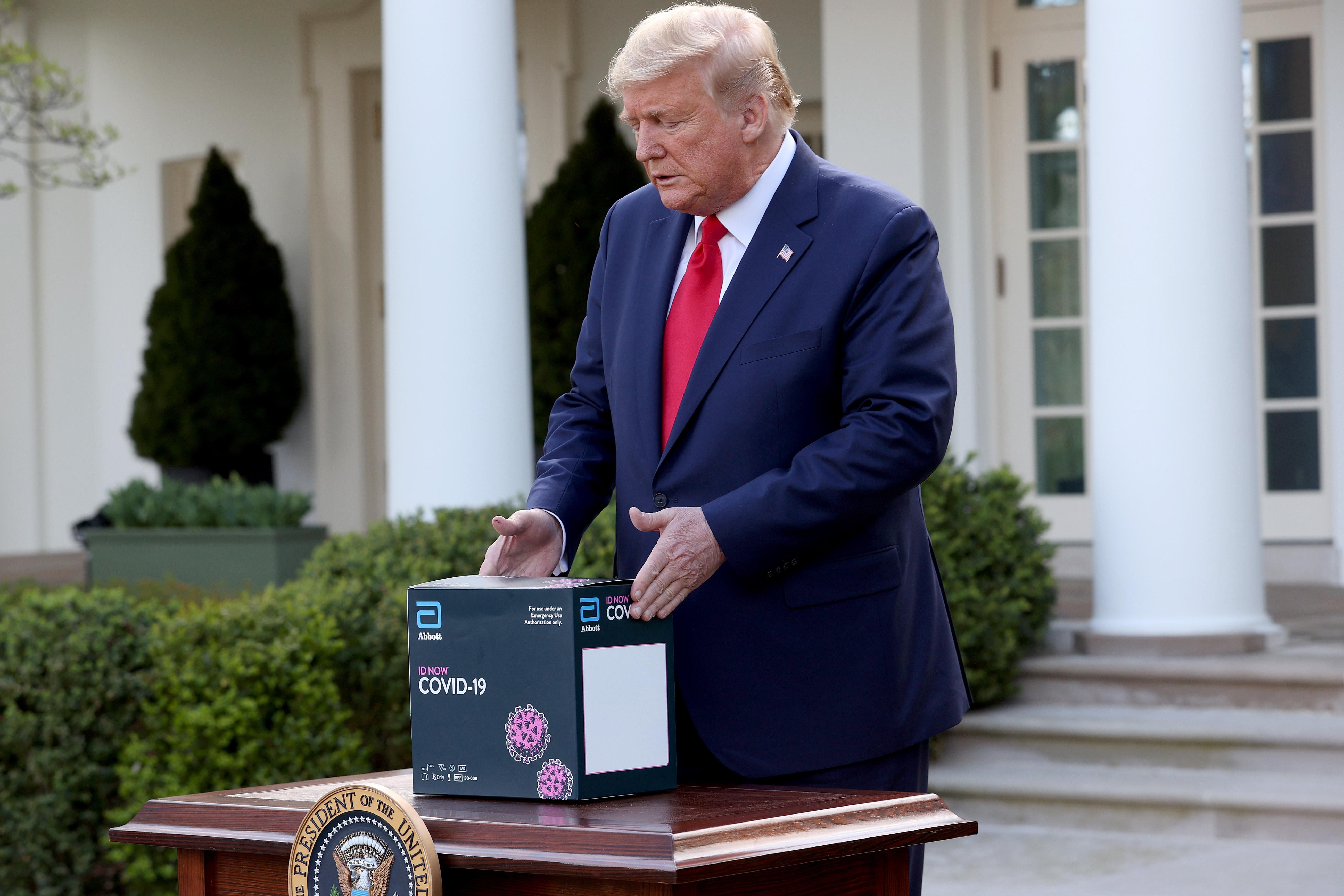 Donald Trump sets down a COVID-19 test kit on a table.