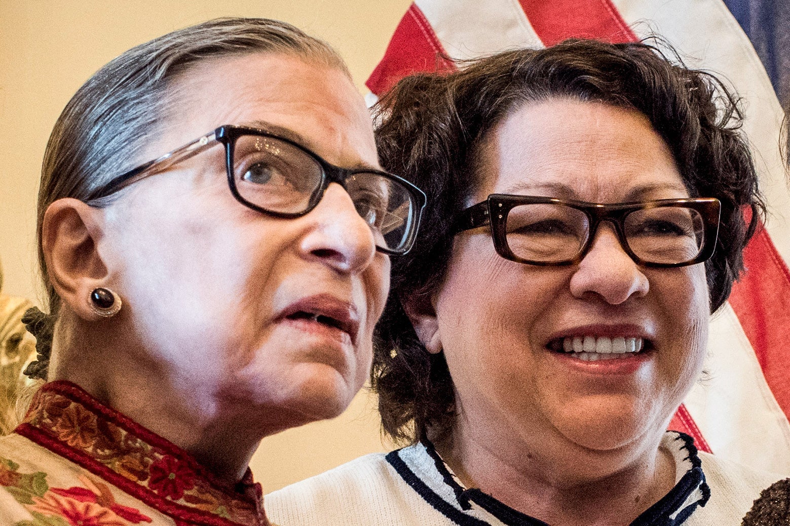 Sotomayor smiles next to Ginsburg, with an American flag in the background.