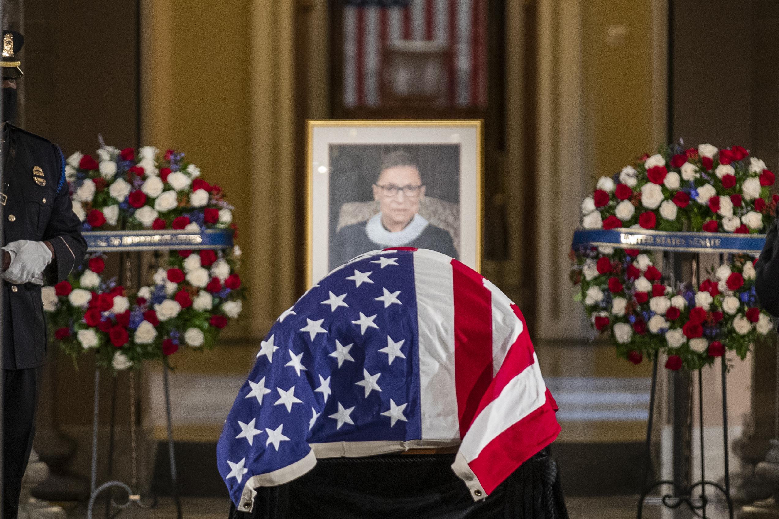 RBG's casket draped in an American flag in front of Ginsburg's portrait flanked by two wreaths.