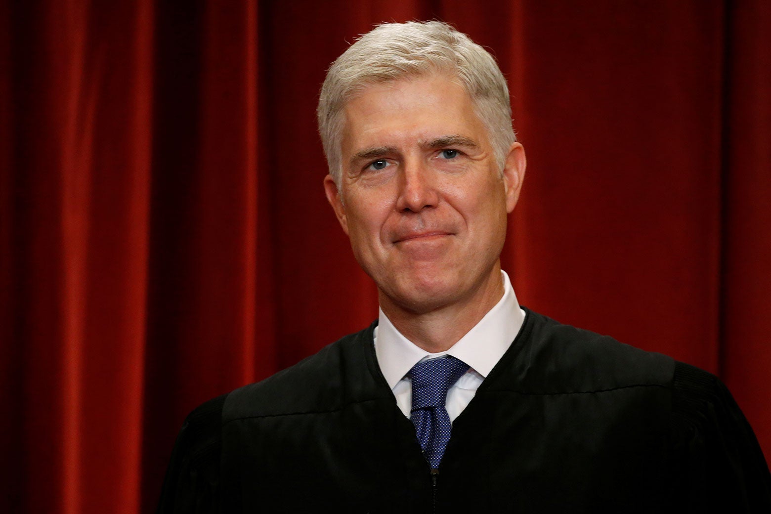 Justice Neil Gorsuch in robes against a red curtain.