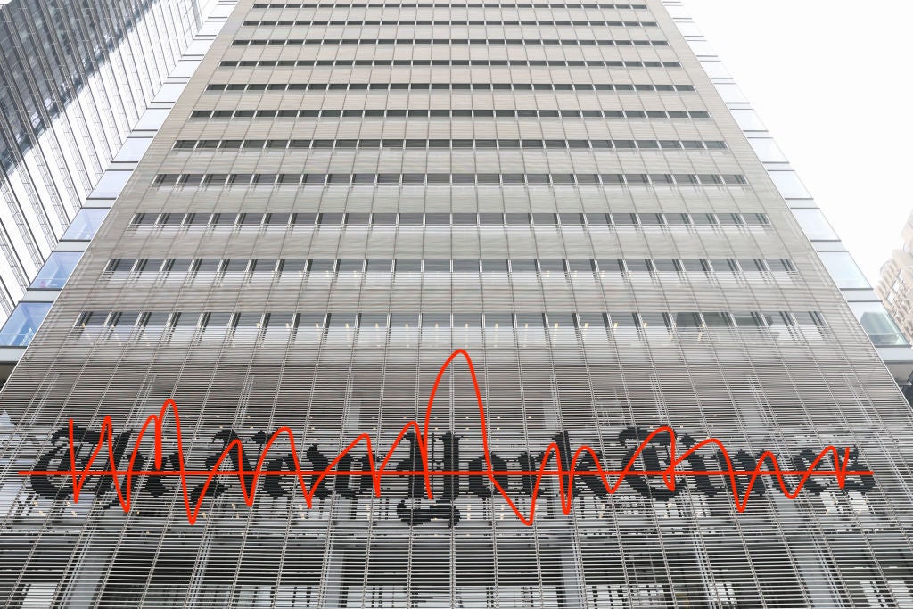 A shot of the New York Times skyscraper headquarters looking up from street level with the "New York Times" sign over the entrance crudely scratched out in red pen.