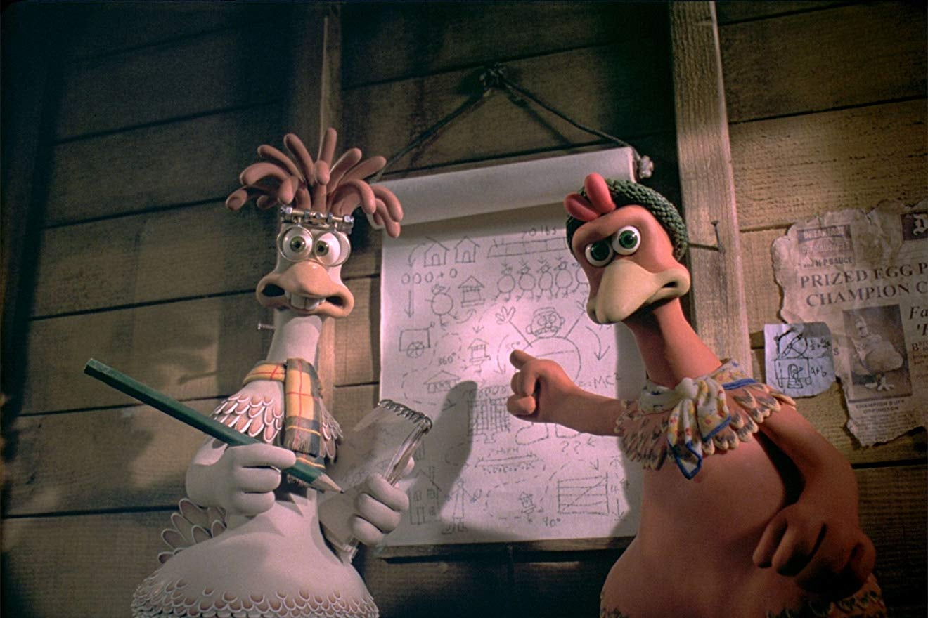 Two stop-motion animated chickens stand in front of a blueprint.