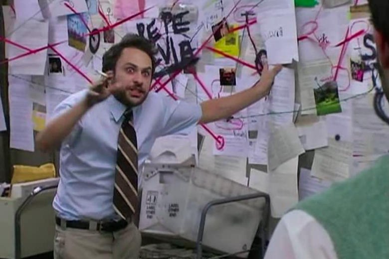 The character Charlie Kelly stands in a mailroom smoking and looking maniacal as he gestures at a wall covered in papers and explains how he's connected a bunch of meaningless dots.