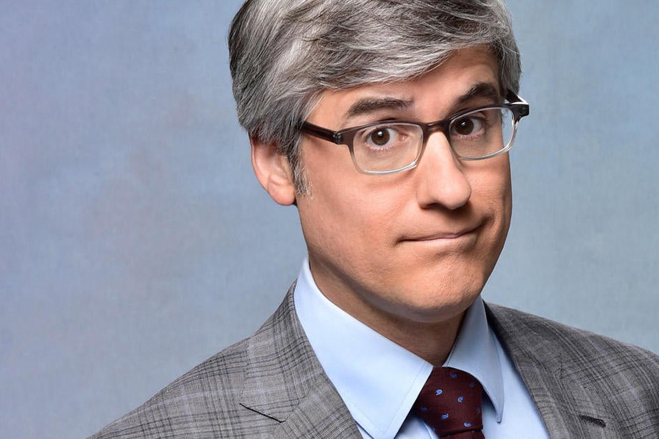 Mo Rocca, cbs news host and author staring toward his audience. 
