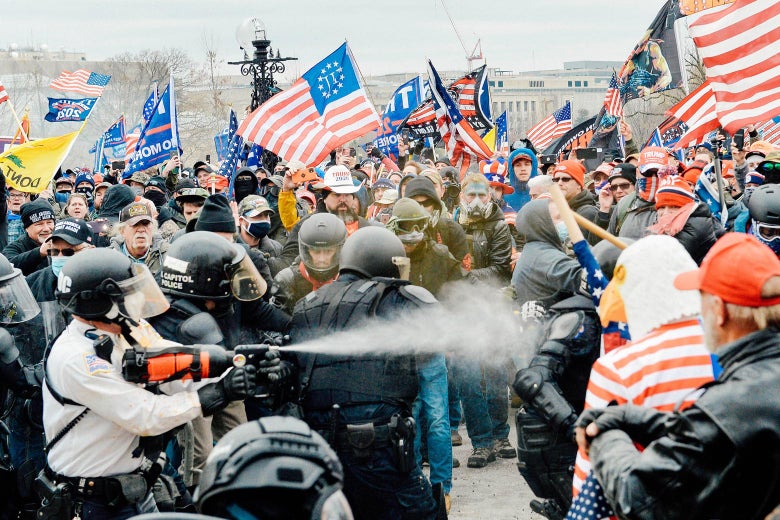 Police spray tear gas into a crowd of people with Trump and U.S. flags.