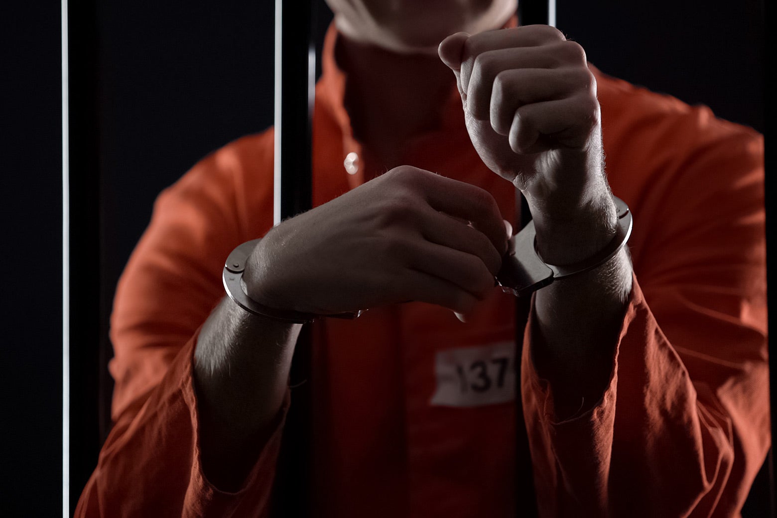 A man behind bars in handcuffs wearing an orange jumpsuit.