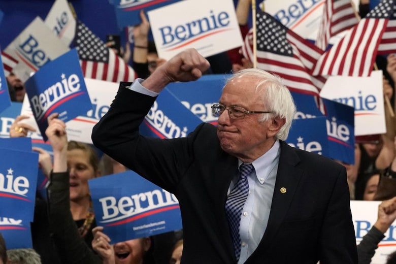 Bernie Sanders raises his fist, with a crowd of supporters behind him.