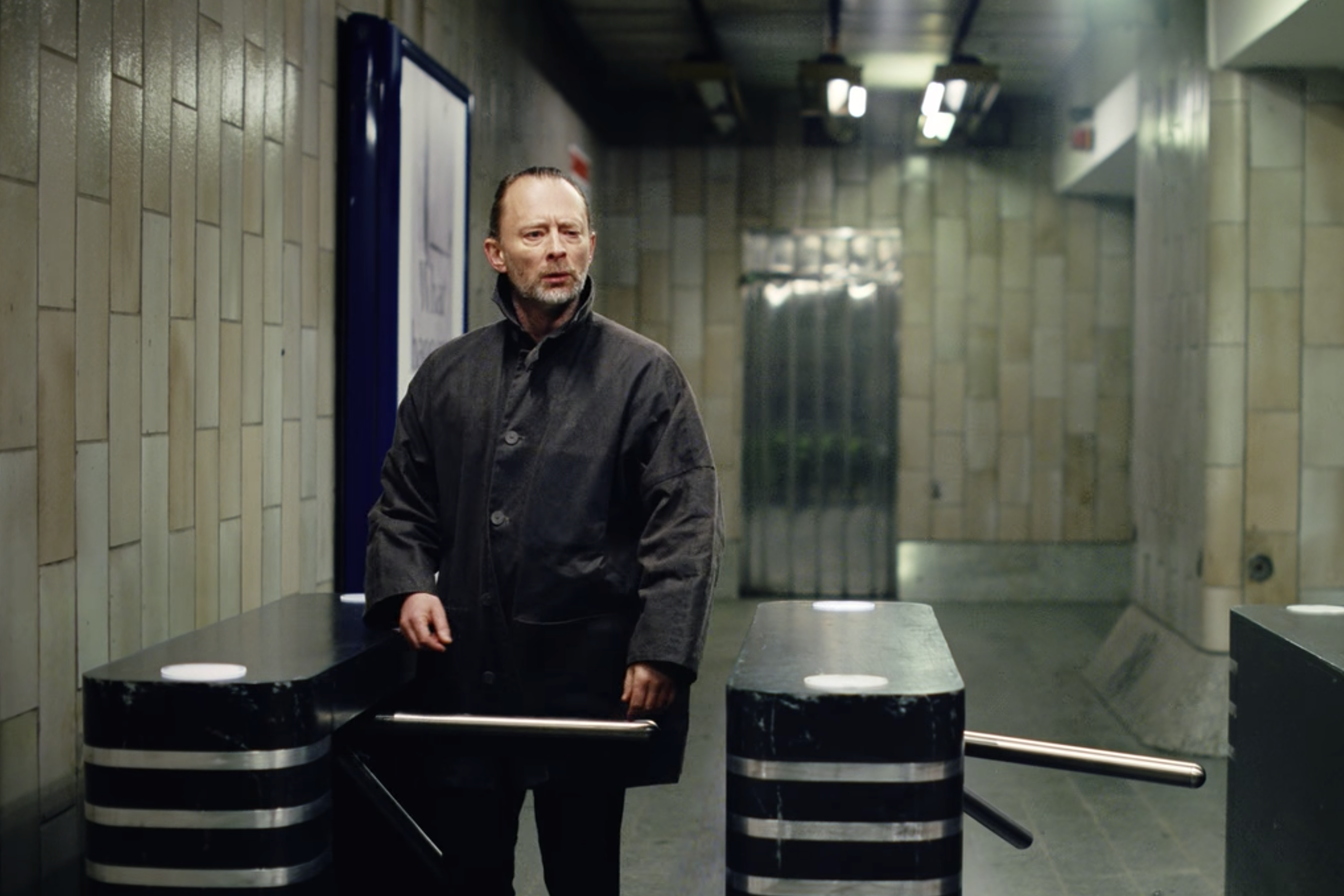 Thom Yorke at a subway turnstile, looking puzzled.