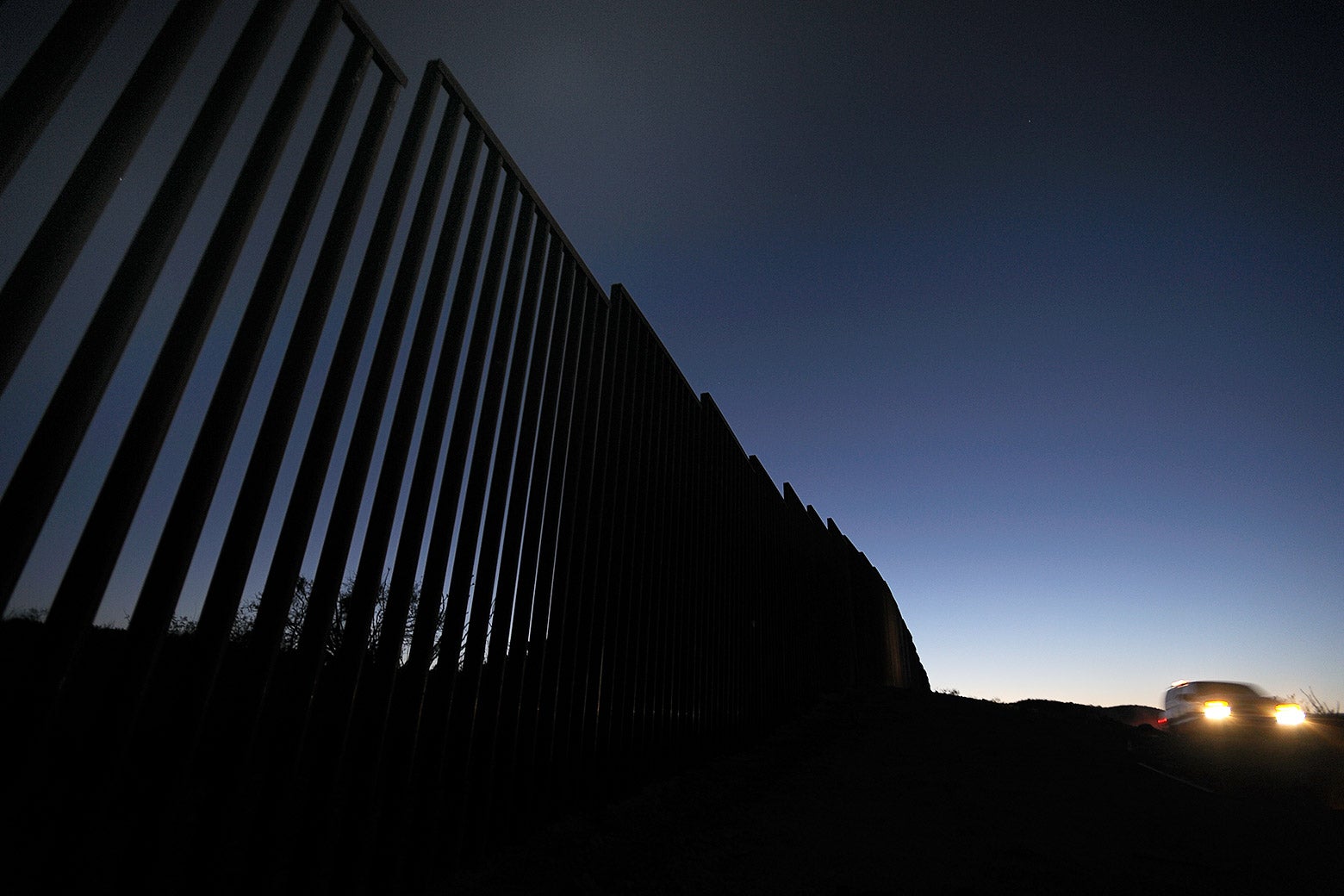 At twilight, a Border Patrol agent drives by a fence at the border.