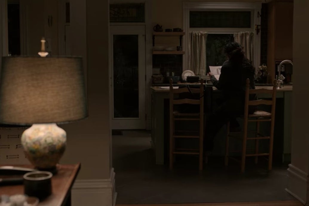 Dr. Kim sits on a tall chair in front of a kitchen counter in a dark house.
