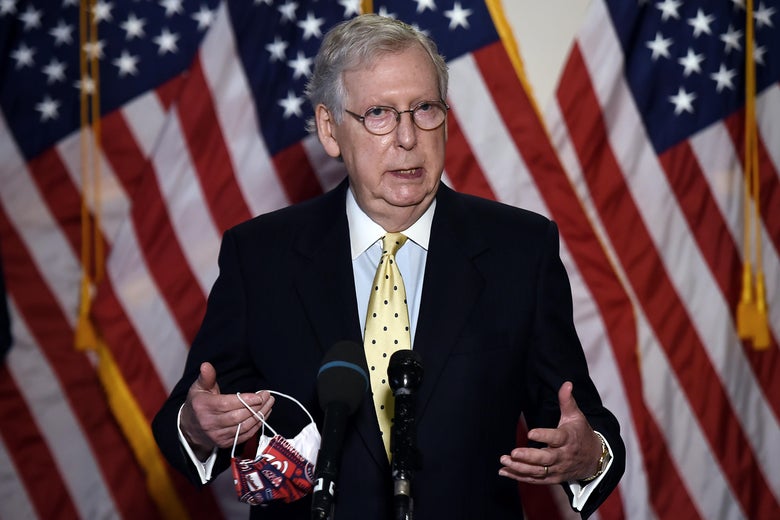 McConnell speaks at a mic, standing in front of American flags