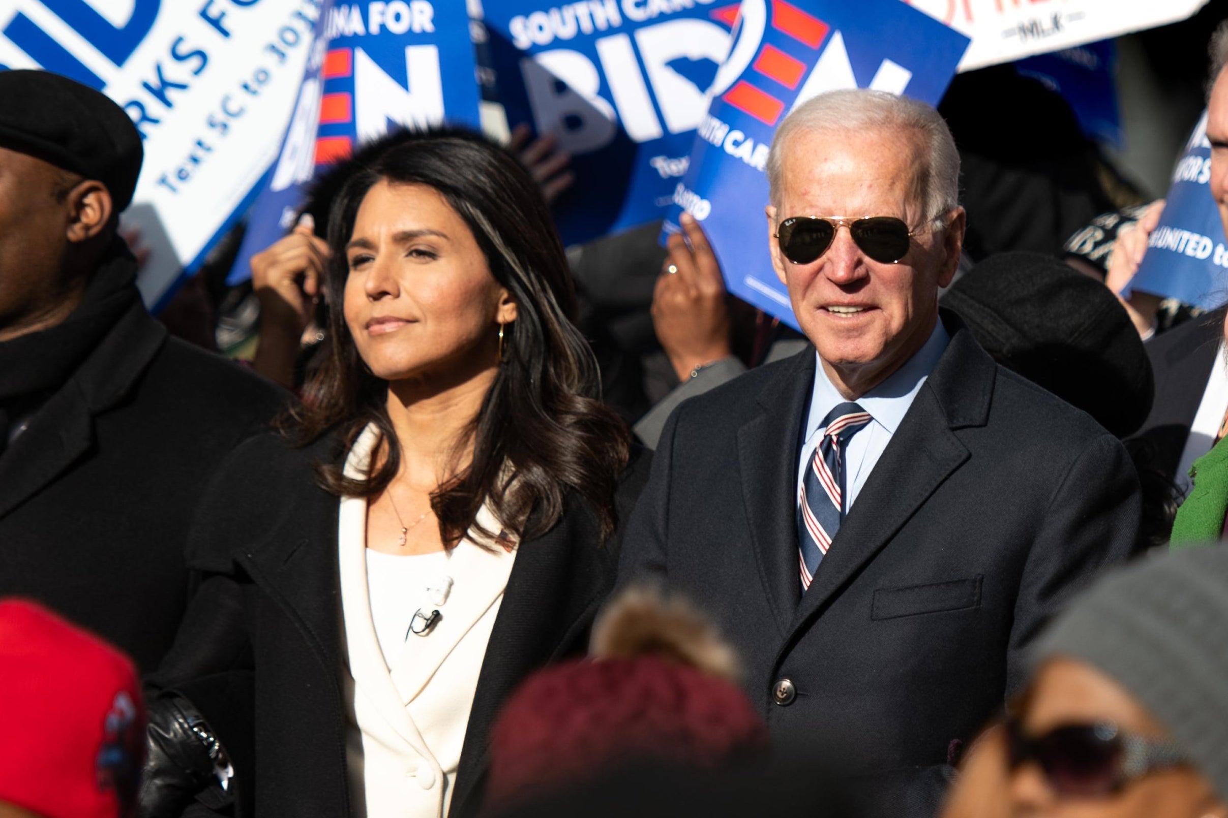 Tulsi Gabbard and Joe Biden march together in the sunshine surrounded by other marchers. Biden is wearing sunglasses.