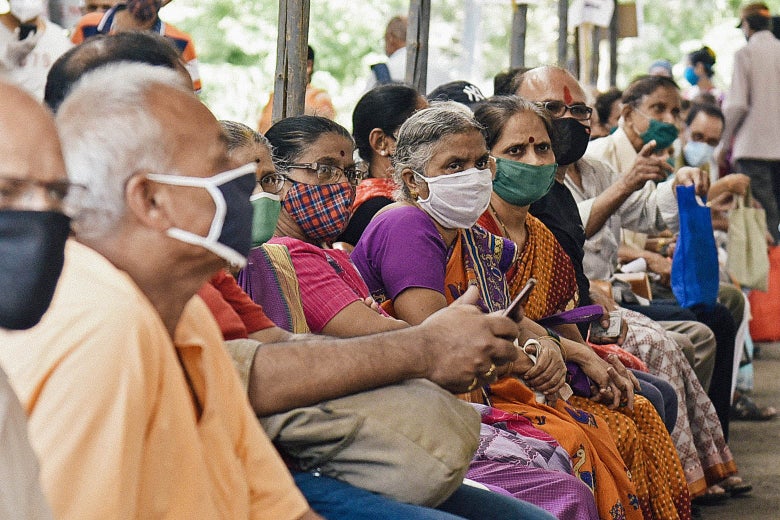 Many people sit close together in line in an open-air vaccination site