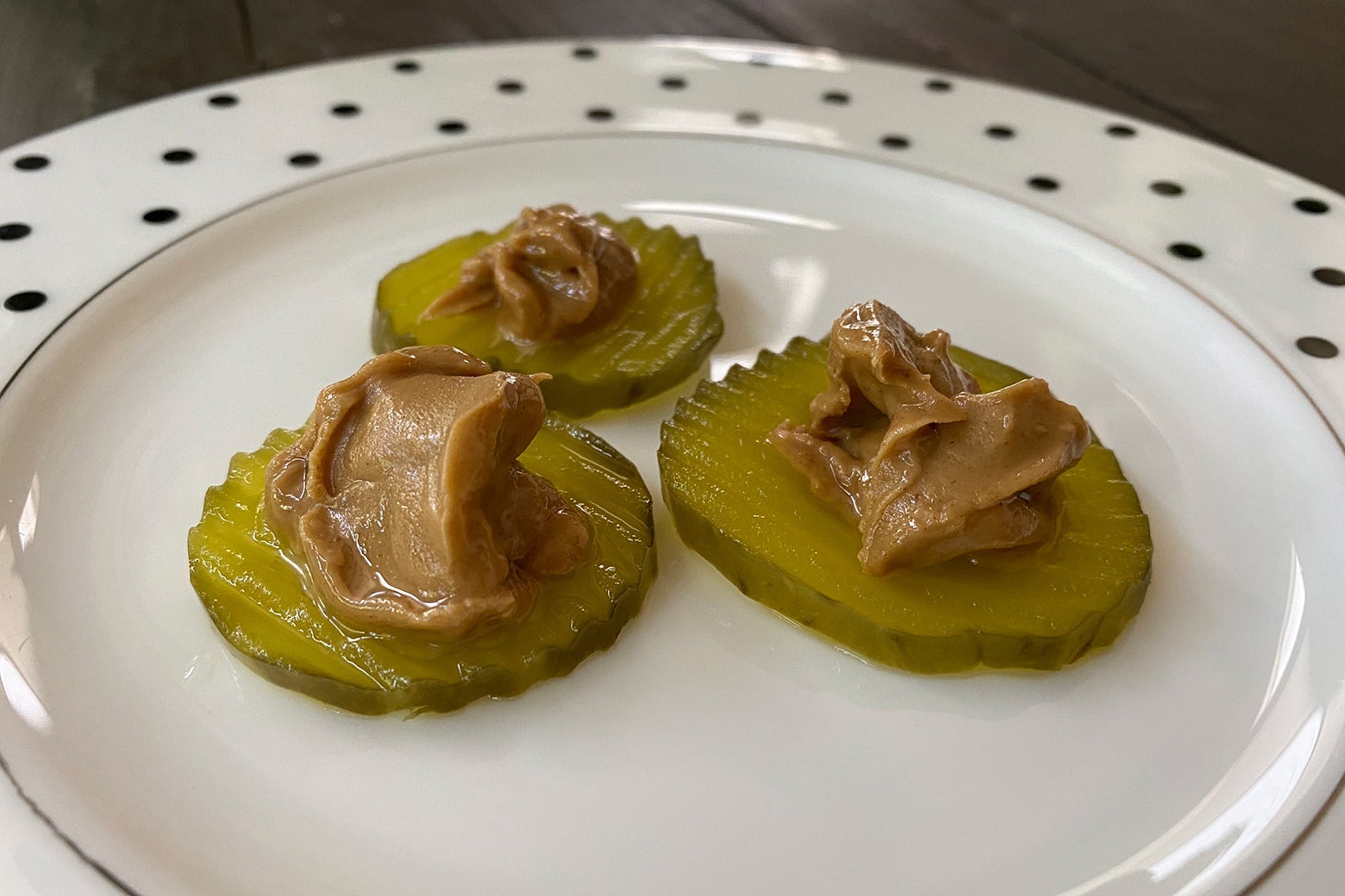 Pickles on a plate with peanut butter on top of them. 