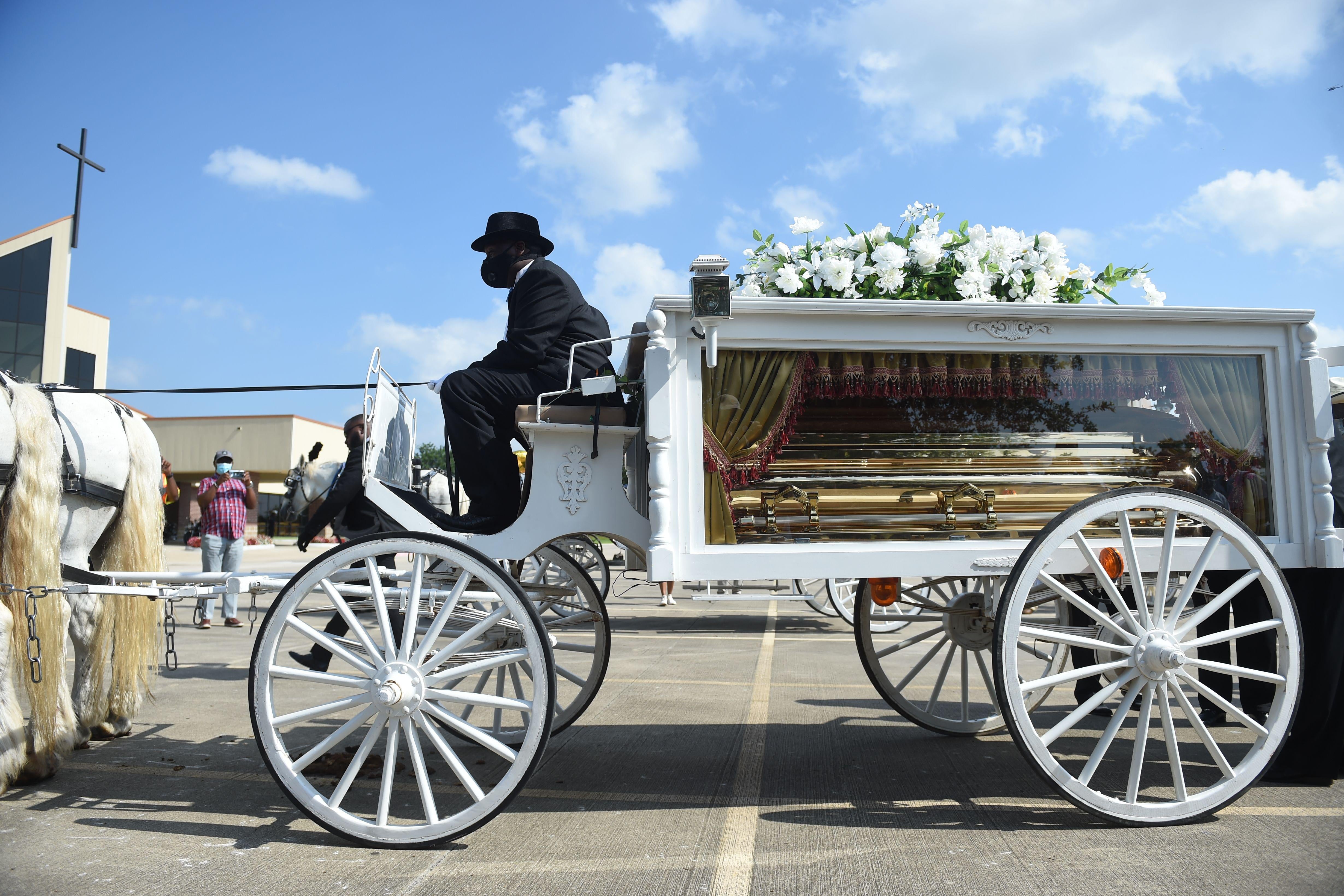 A horse and buggy carry a glass box holding the casket of George Floyd.