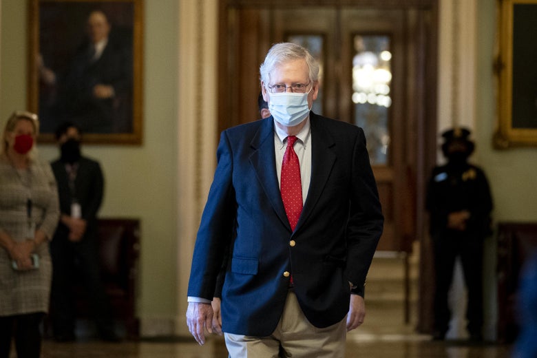 Mitch McConnell, wearing a medical mask, walks through a room in the U.S. Capitol