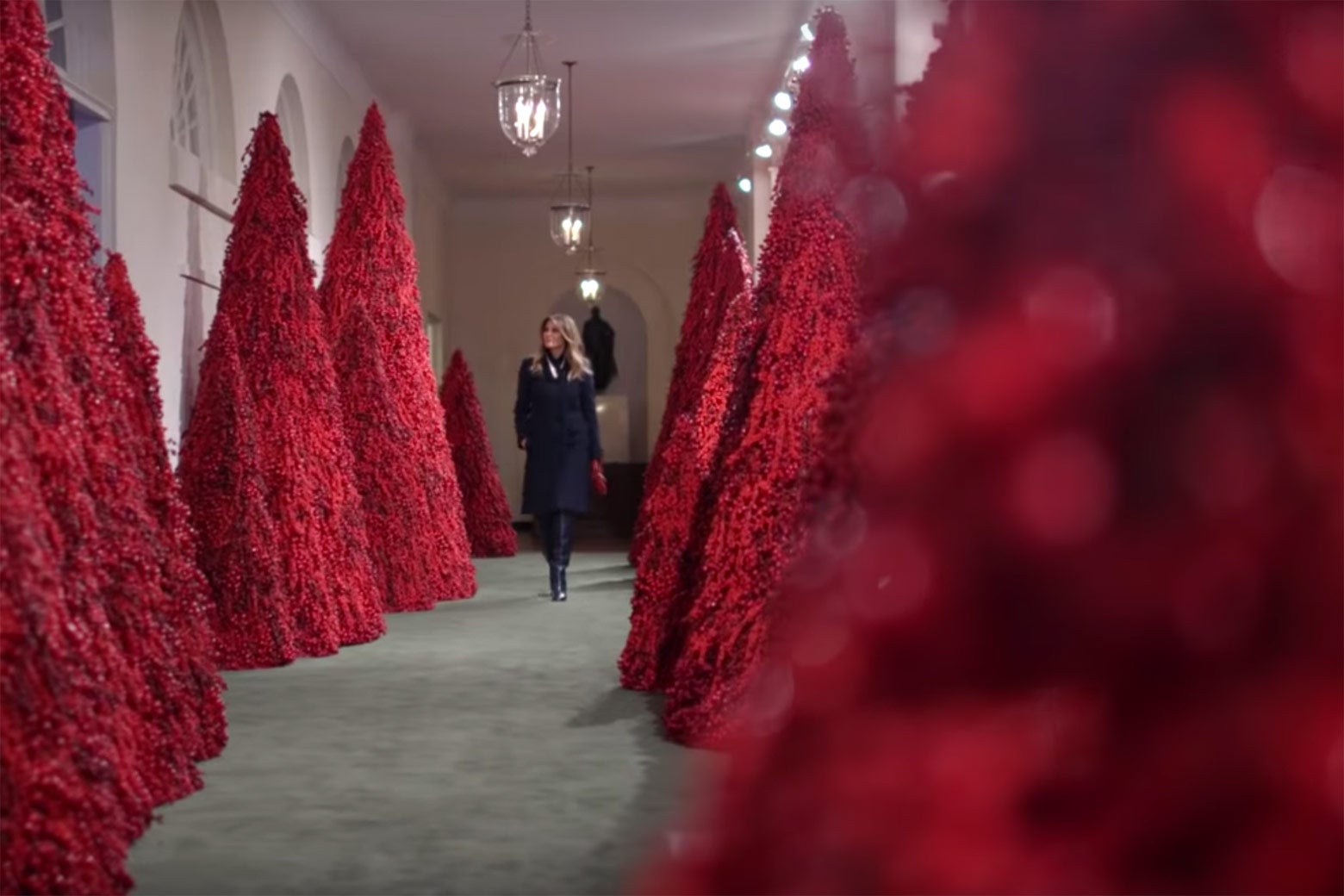 Melania Trump walks down a hallway lined with giant red textured cones.
