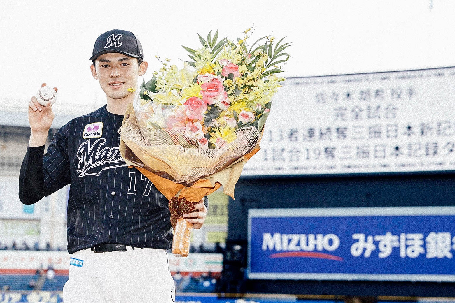 Pitcher Roki Sasaki holds a baseball and a bouquet of flowers.