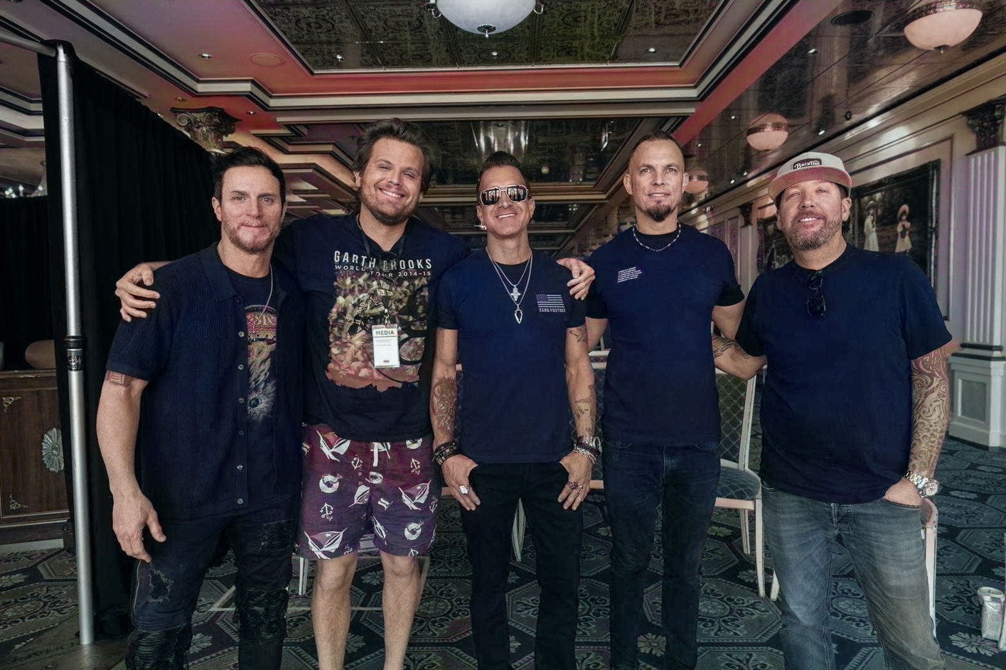 Band members pose with Luke, who wears a Garth Brooks T-shirt, in a cruise ship ballroom.