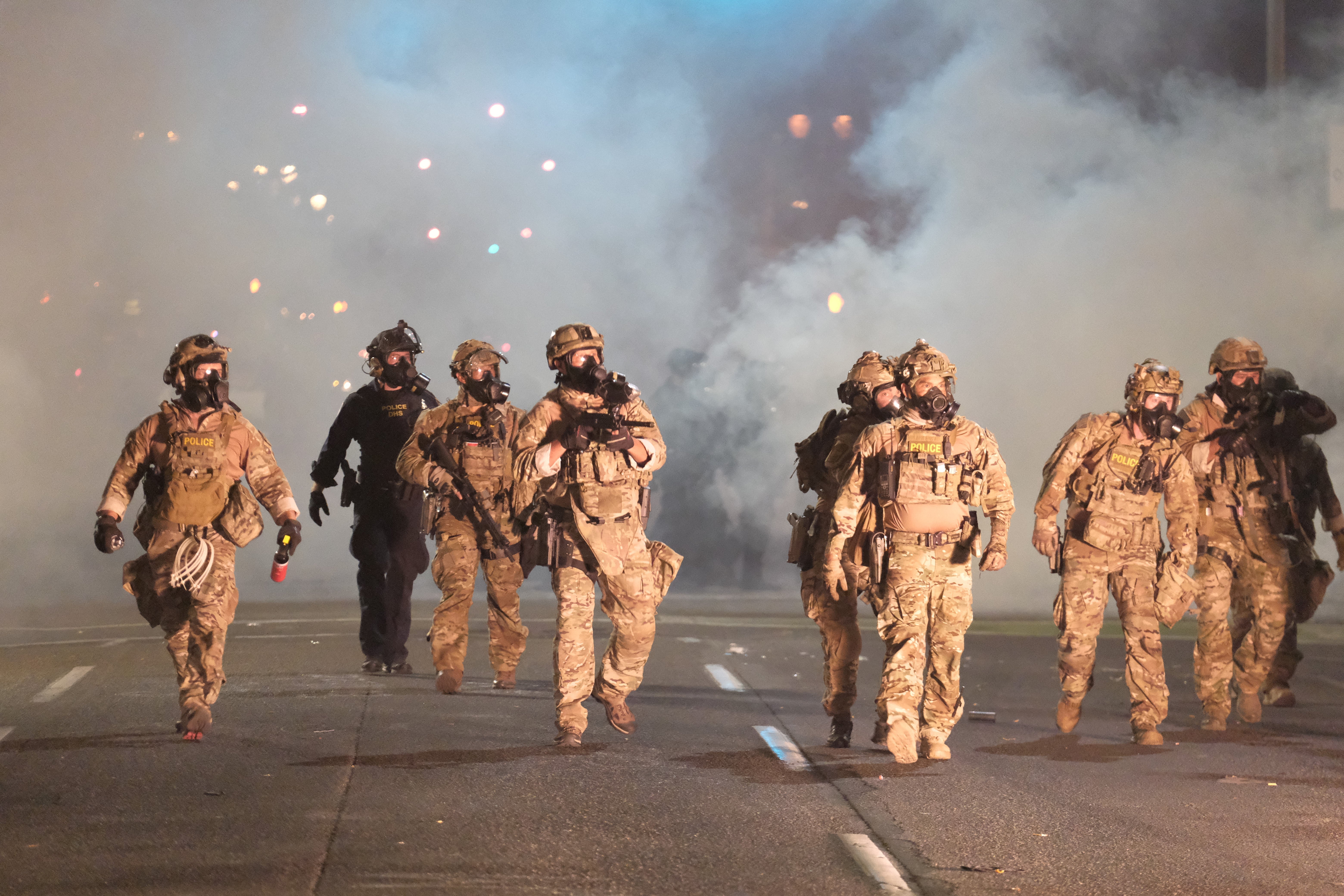 Officers in camo walk down a street at night amid smoke.