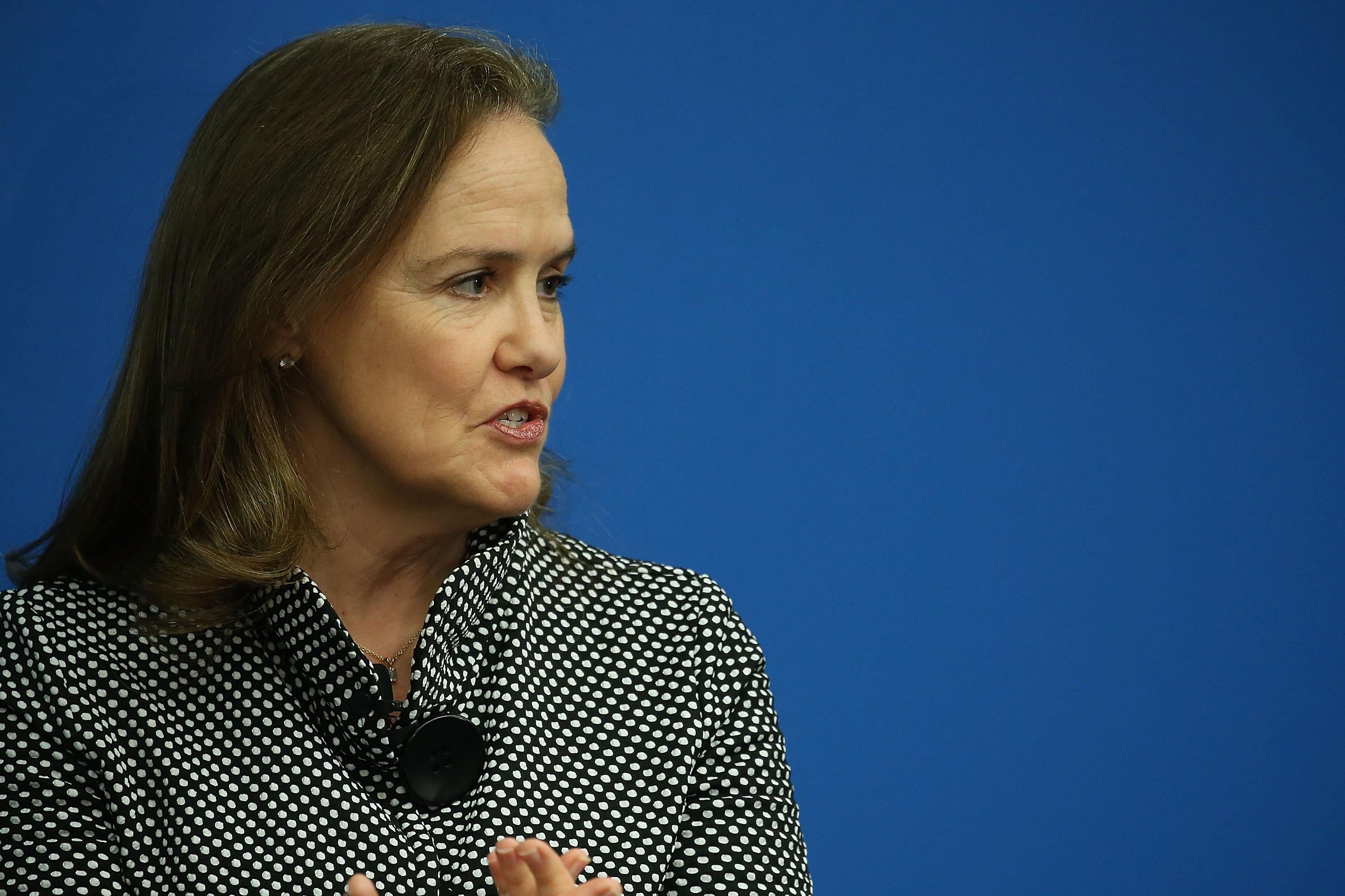 Flournoy gestures with her hands while speaking in front of a blue background.
