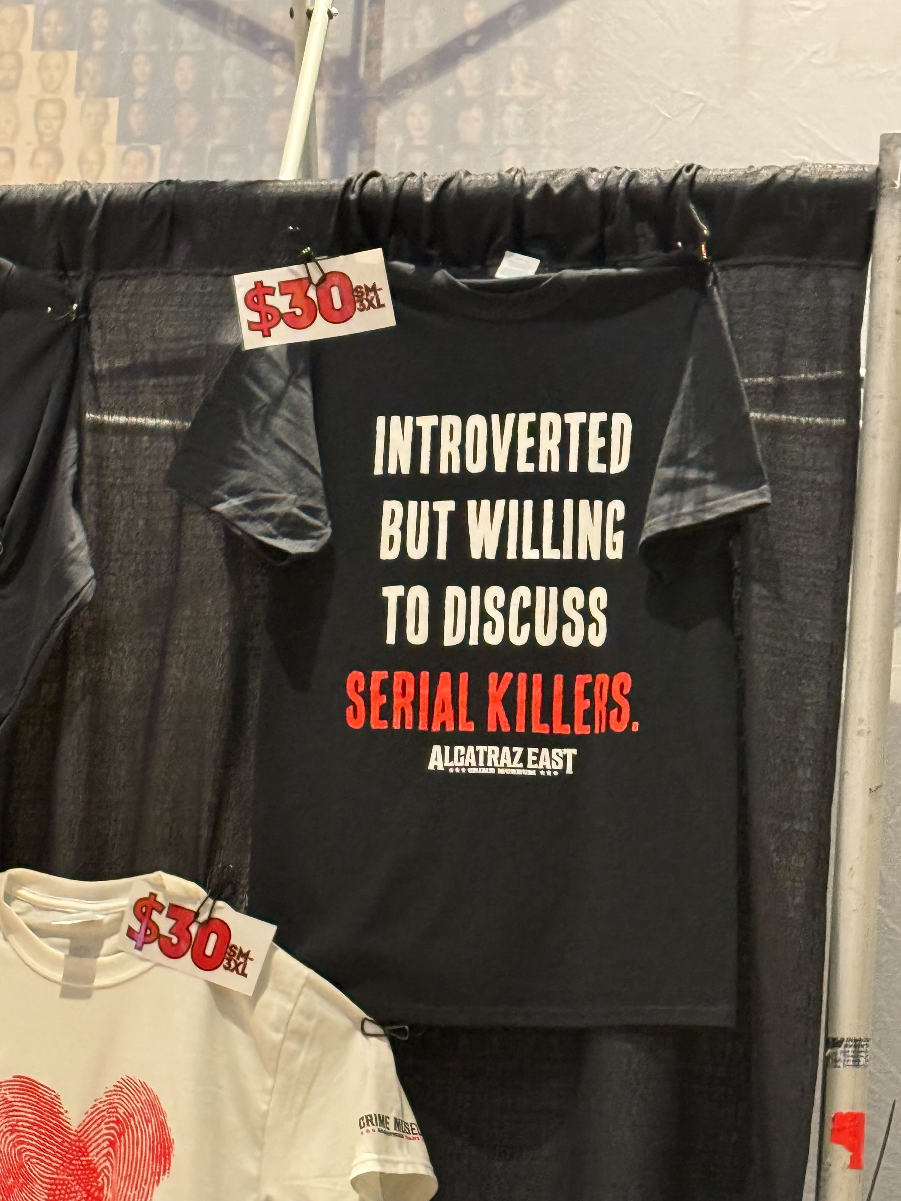 CrimeCon merch for sale, including black T-shirts that say "Introverted by Willing to Discuss Serial Killers."