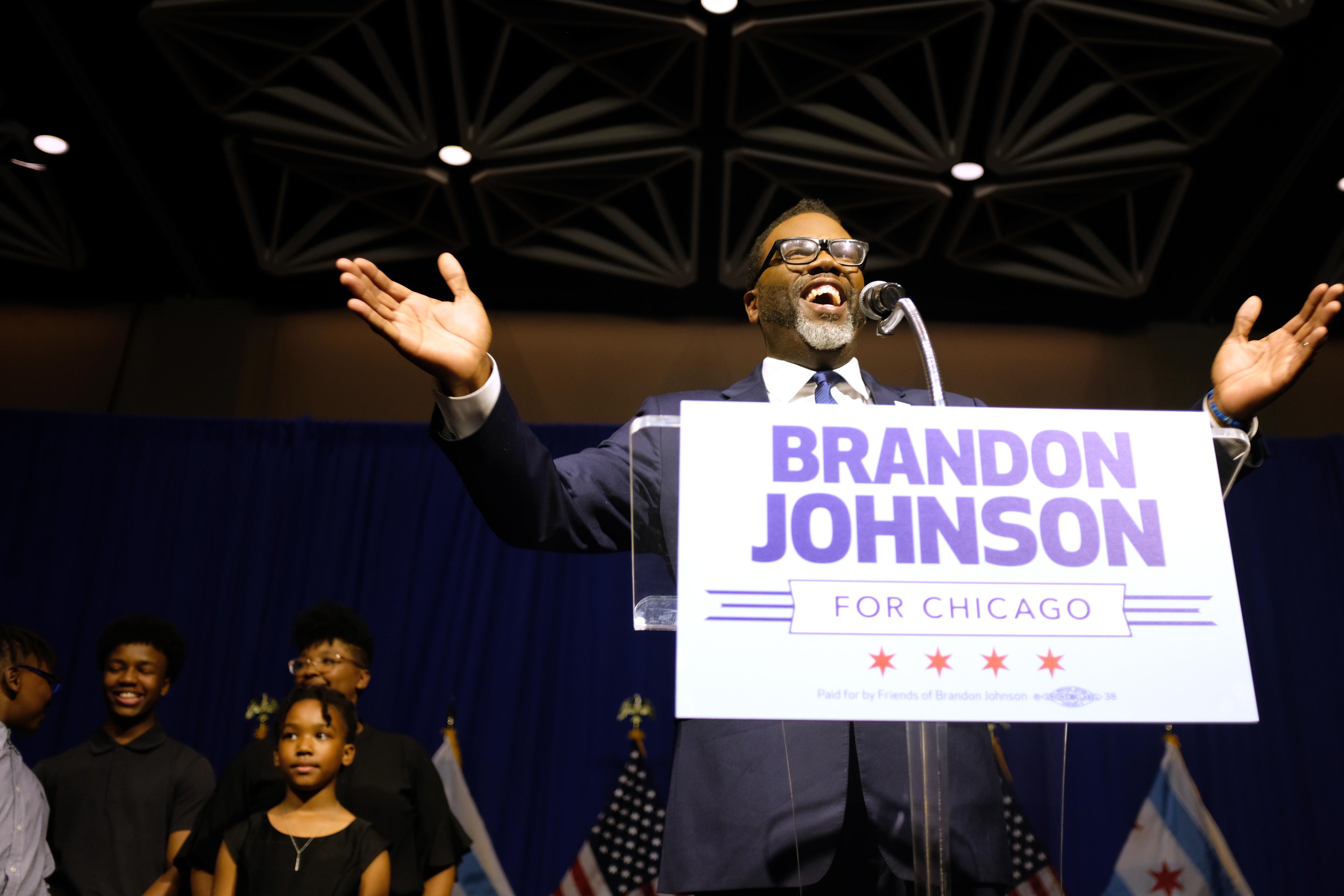 Brandon Johnson speaks after being projected winner as mayor. He's smiling and standing behind a sign bearing his campaign logo.