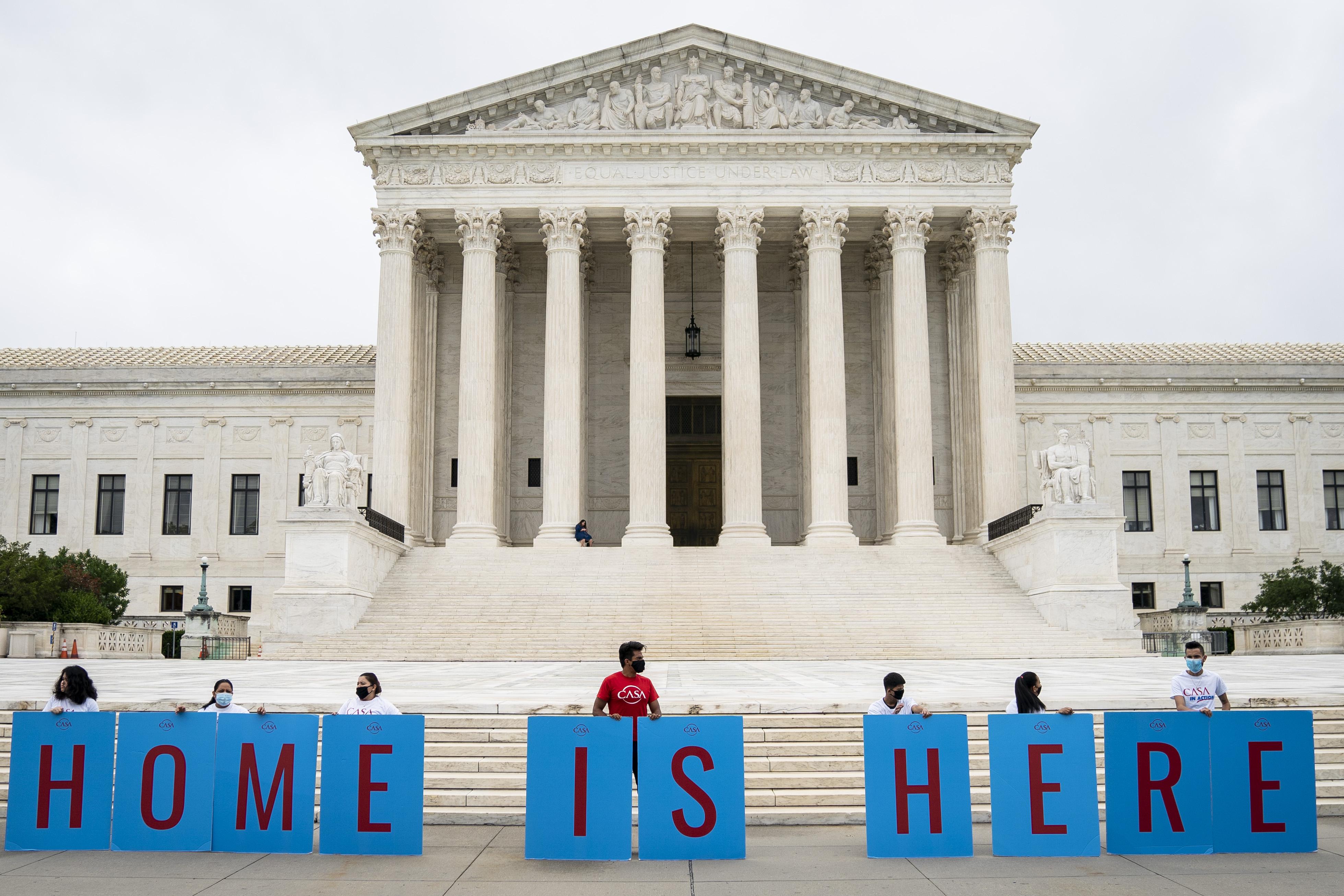 Activists hold signs that together read "Home is here" in front of the Supreme Court building