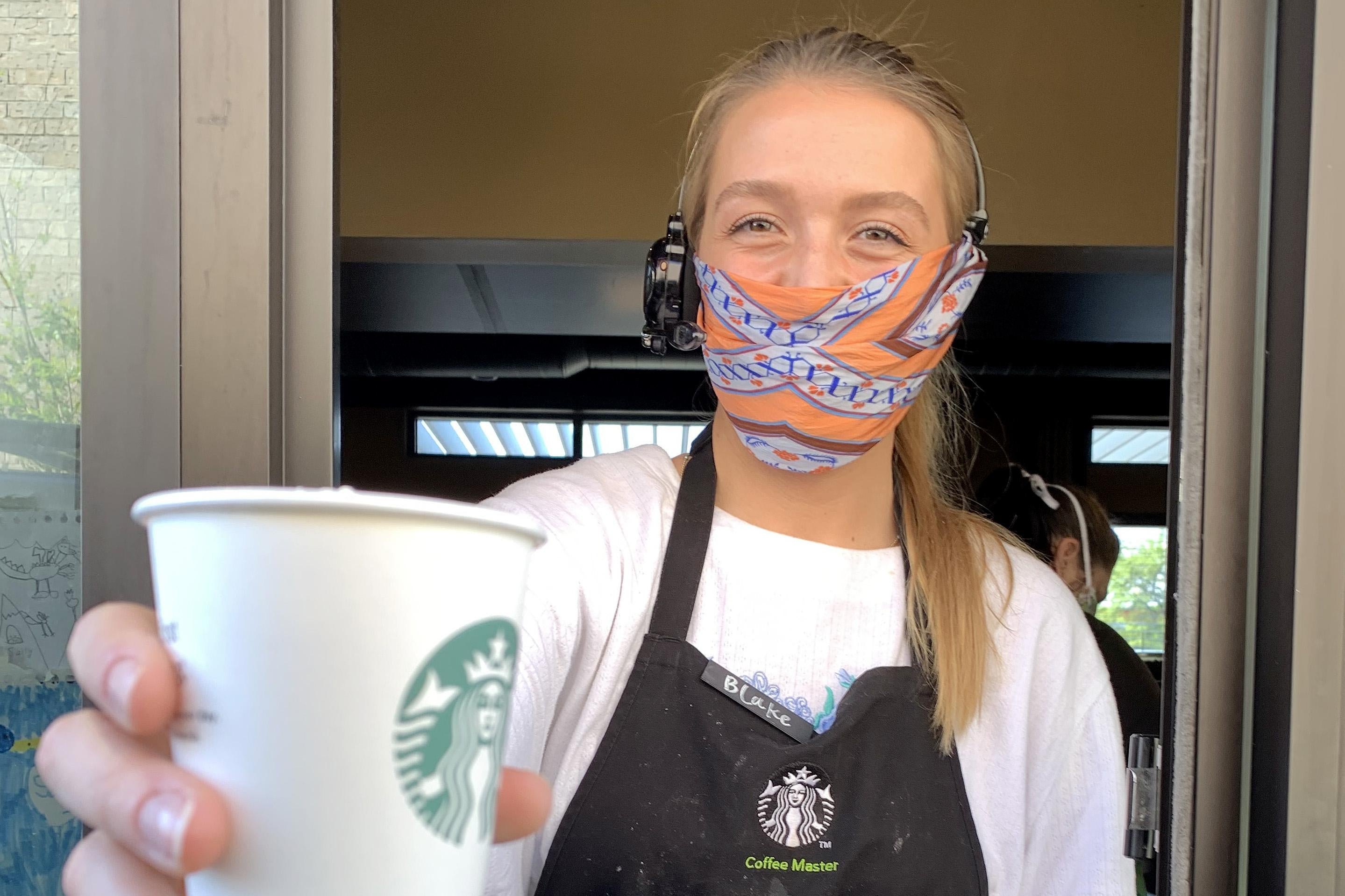 A Starbucks employee wears a facial covering while working the drive-thru during the coronavirus (COVID-19) pandemic on April 07, 2020 in Dallas, Texas.  Starbucks is requiring employees to wear a facial covering and is making thermometers available to employees who would like to take their temperature before starting a shift. 