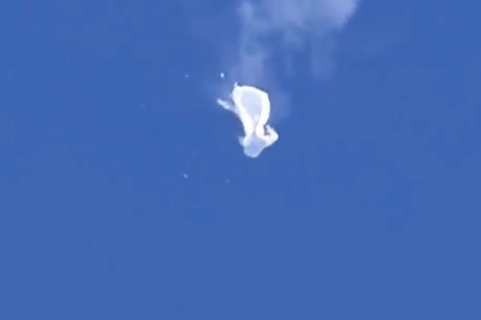 A balloon, deflated, hangs in the blue sky, losing altitude.