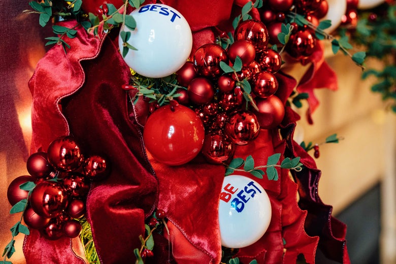 White ornaments that say "Be Best" are surrounded by red ribbons, fake holly berries, and red Christmas balls.
