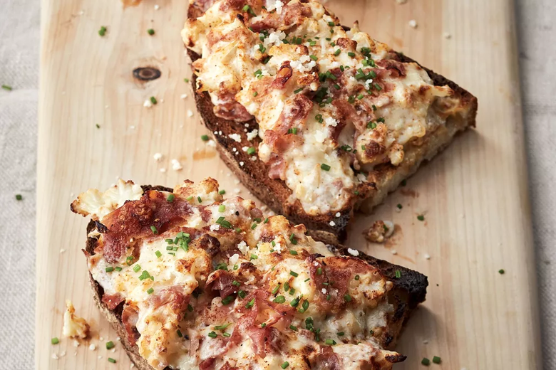 Two toasted slices of country-style bread topped with cauliflower, cheese, and prosciutto