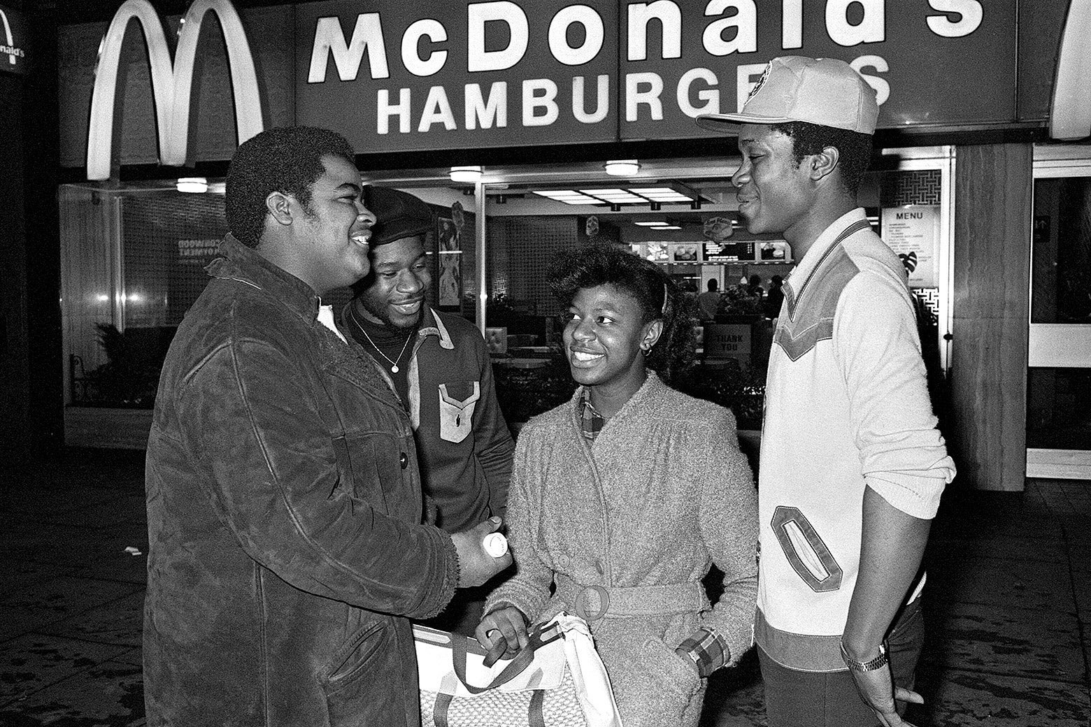 Black-and-white photo of four black teens smiling and standing outside a McDonald's.