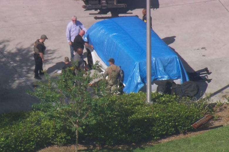Men surround a white van that's covered with a blue tarp in what appears to be a still from a video shot by a news helicopter.