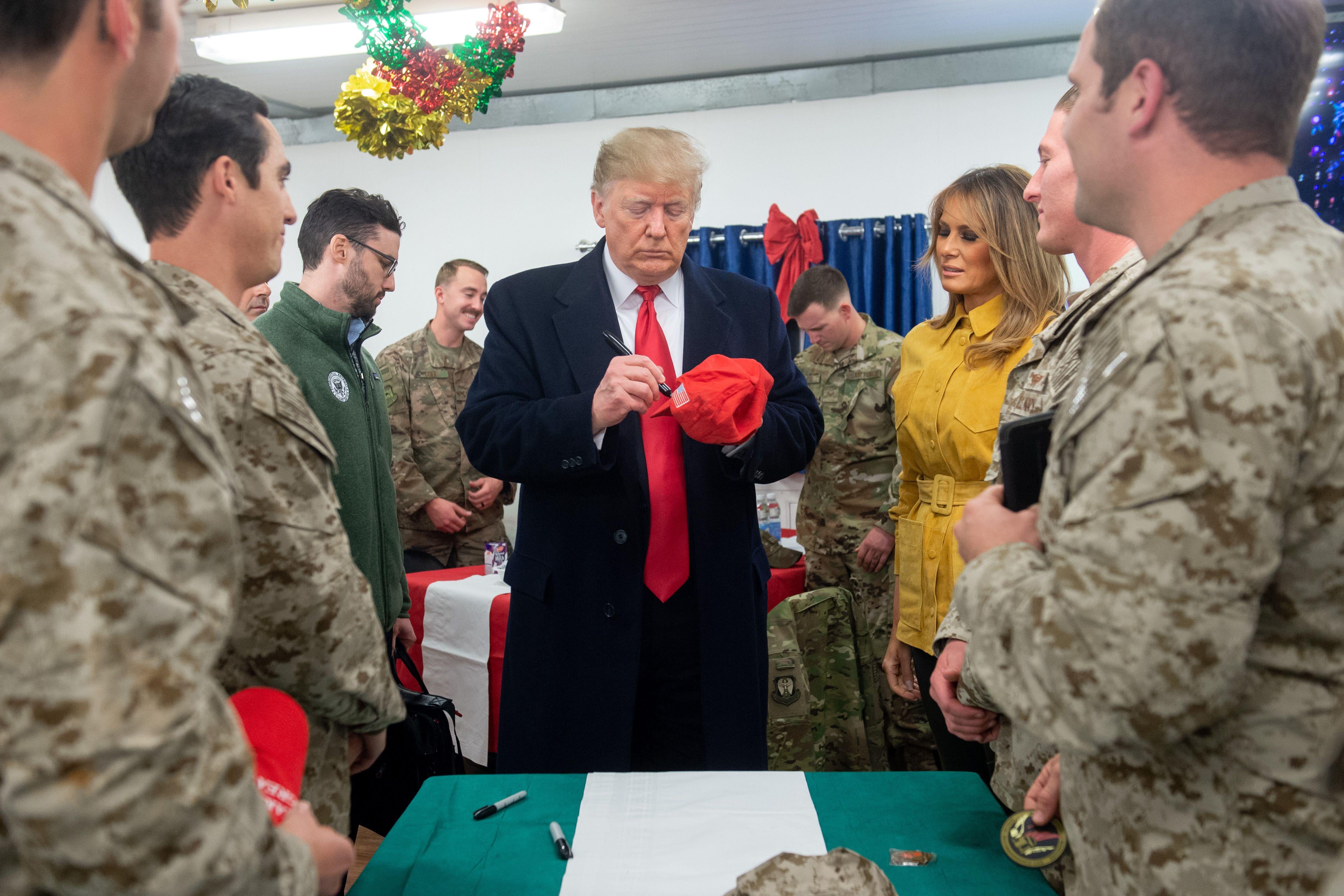 President Donald Trump signs a hat as First Lady Melania Trump looks on as they greet members of the U.S. military during an unannounced trip to Al Asad Air Base in Iraq on December 26, 2018.