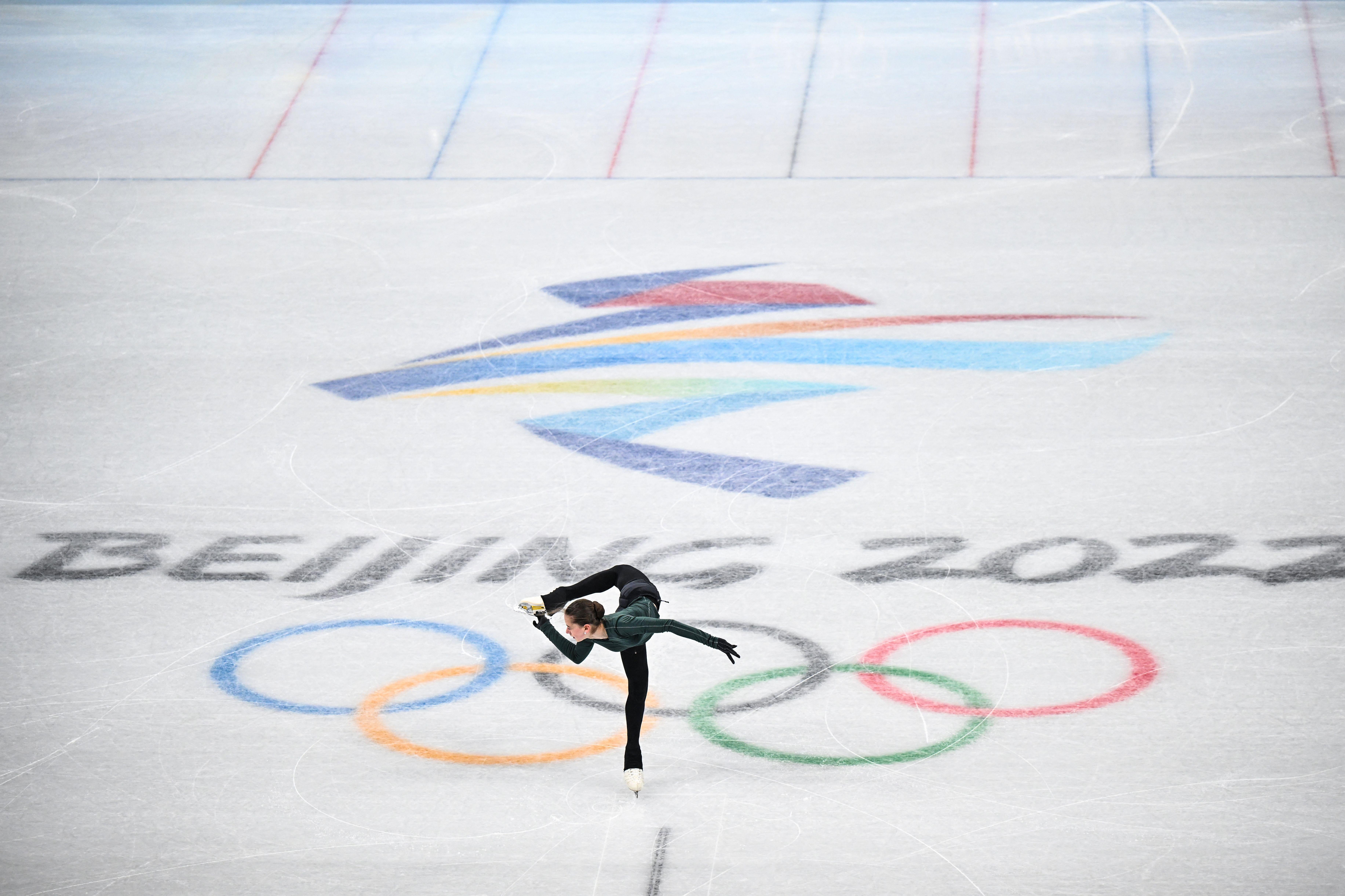 A figure skater contorting herself with her leg above her head, with the Beijing 2022 and Olympic rings logos on the ice.
