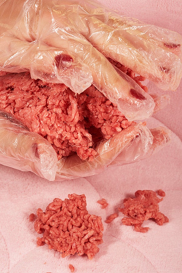 A woman wearing clear gloves handling ground beef.
