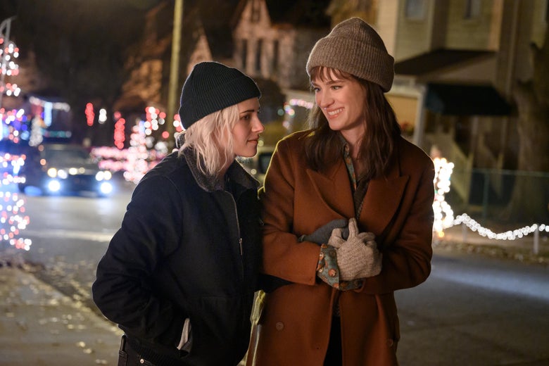 The two women hold hands while walking down a festive street in cozy knitwear