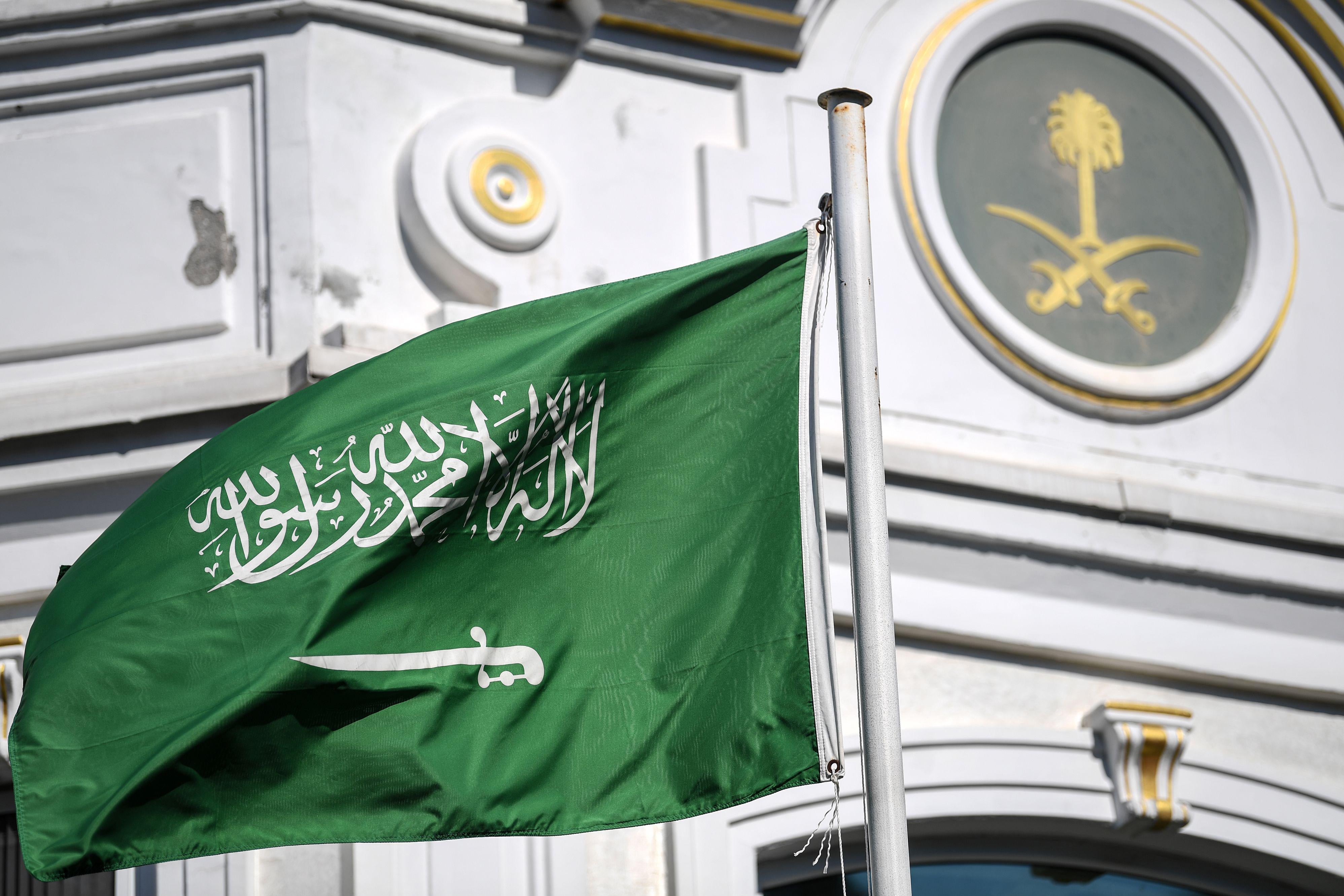 The flag of Saudi Arabia in front of an ornate building.