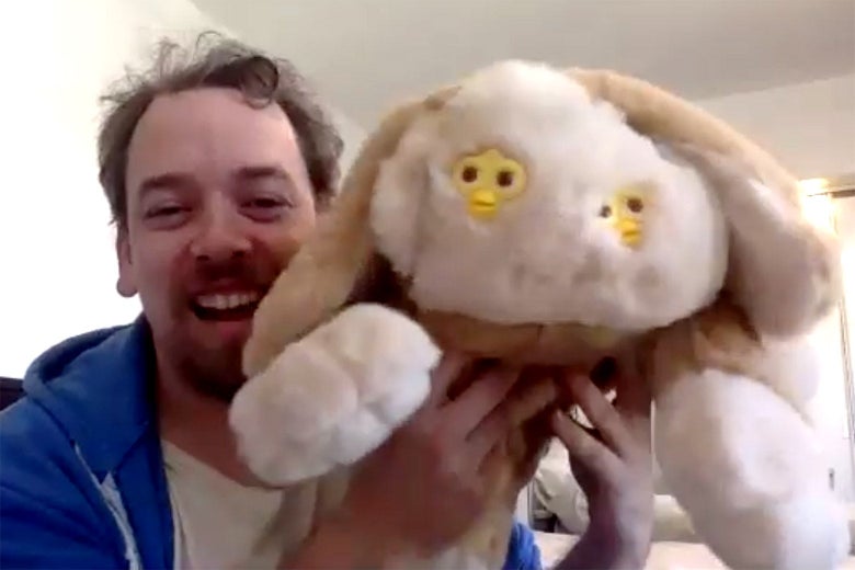 Mike Rianda holding a doll that looks like a dog with two Furby faces.