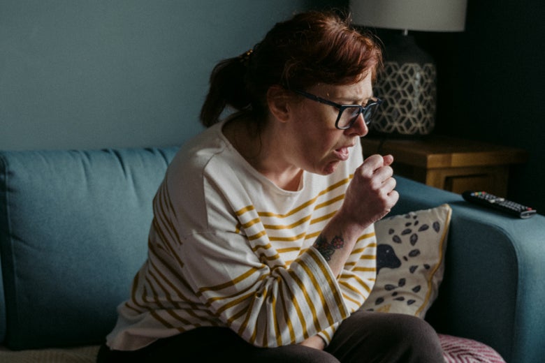 A woman sitting on a couch coughs.