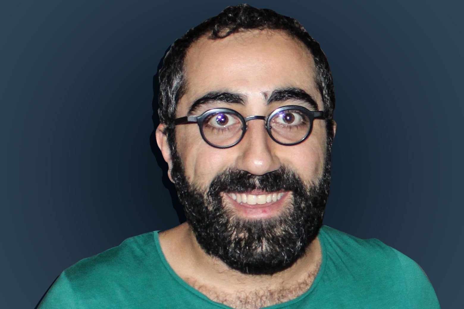 A bearded man in black glasses smiles while wearing a green T-shirt.