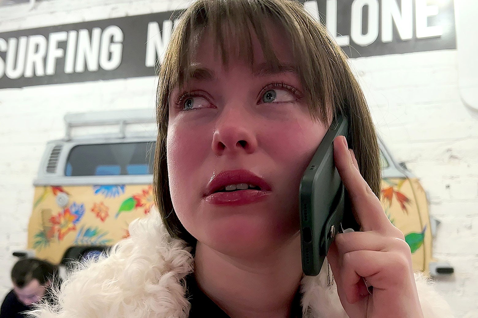 A twentysomething white woman with a bob speaks into a phone, looking nervous.