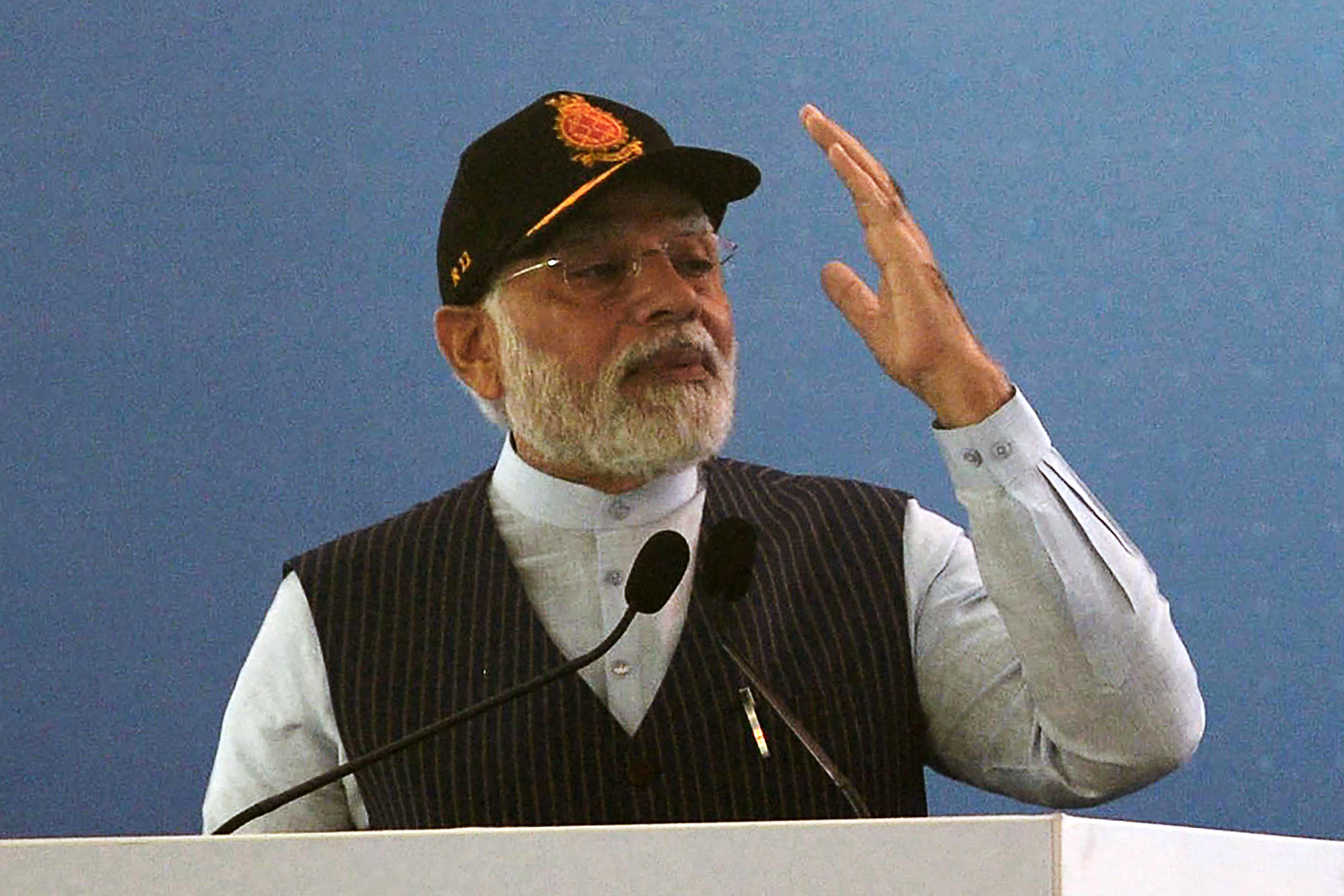 A man in a vest and baseball cap gestures with his arm as he speaks at a lectern.