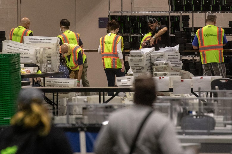 People in yellow vests stand around clear plastic mail crates.