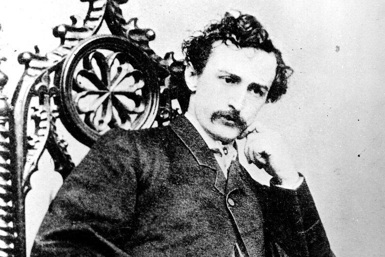 John Wilkes Booth sitting in a chair with his chin resting on his left hand.