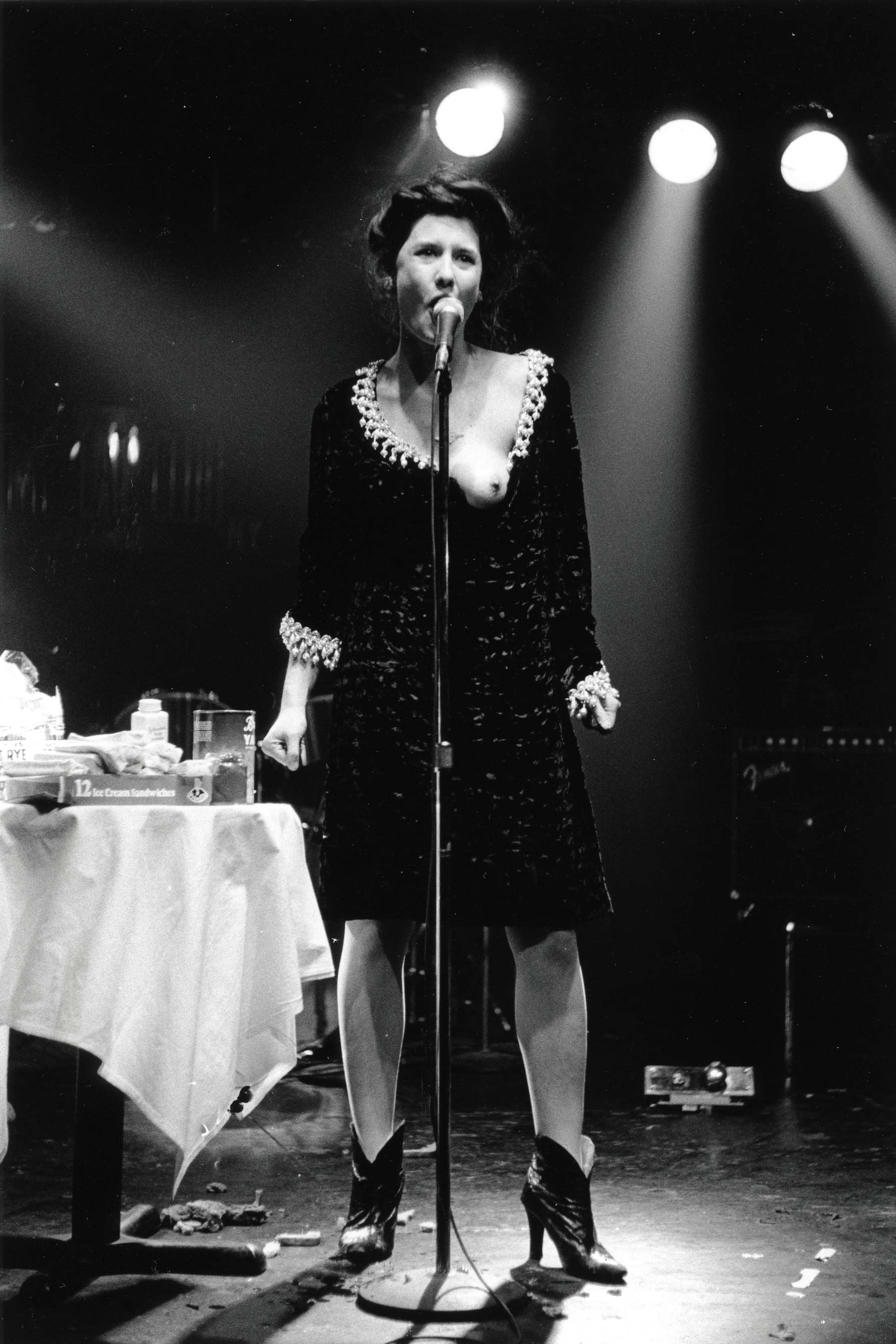 Karen Finley speaks into a microphone with one breast exposed.