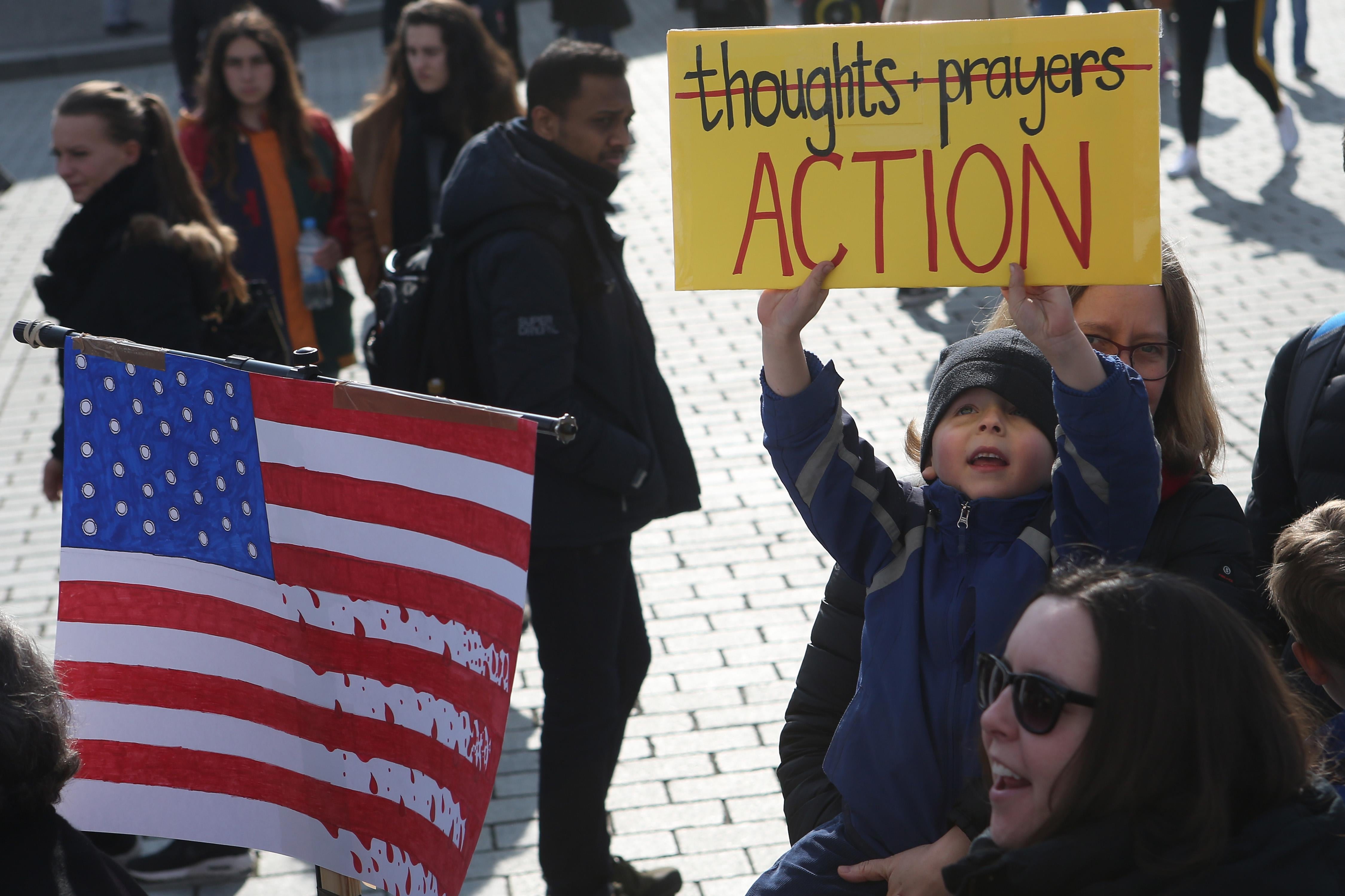 A child holds a sign in which the words thoughts & prayers have been crossed out. Below that reads, "Action."