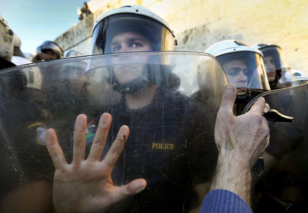 A protester places his hand against the shields of riot policeme
